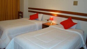 Two single beds with white bedding and red pillows, a nightstand with a lamp, and a wooden headboard. - CUSCO HOUSE HOTEL (Cusco)