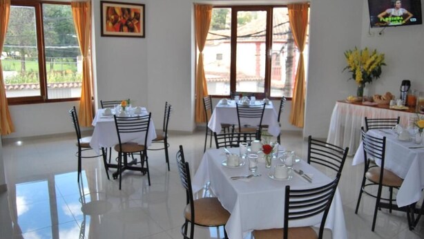 A dining area with tables set for four, chairs, and a TV mounted on the wall. - CUSCO HOUSE HOTEL (Cusco)