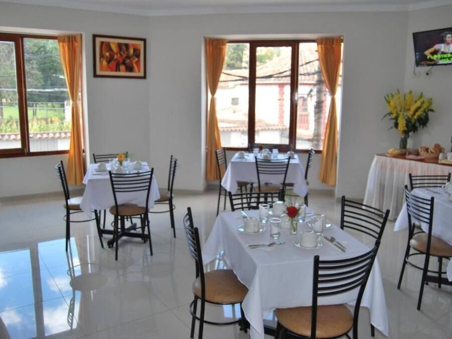 Un comedor con mesas dispuestas para cuatro personas, sillas y un televisor montado en la pared.