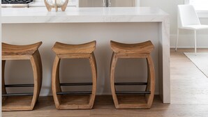 Una cocina moderna con encimera blanca, electrodomésticos de acero inoxidable, taburetes de madera y una lámpara colgante.