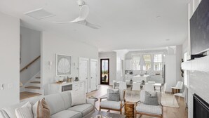 Una sala de estar moderna con un sofá, una mesa de centro y sillas. Se ve una escalera que lleva a otro nivel, un área de cocina y un comedor.