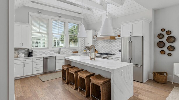 Una cocina moderna con armarios blancos, una isla grande con taburetes, un refrigerador de acero inoxidable y un tragaluz.
