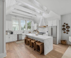 A modern kitchen with white cabinetry, a large island with stools, a stainless steel refrigerator, and a skylight. - Stylish Cottage in Moreland walk to everything (Bluffton)