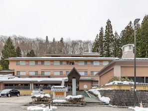 A multi-story hotel with a snow-covered roof and a small entrance with a sign. - Hanayama Onsen Nuruyusanso Tabist (Kurihara)