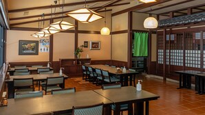 Un restaurant avec des tables et des chaises en bois, des suspensions décoratives et un rideau vert.