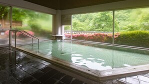 Une piscine intérieure avec des parois en verre transparent, une rampe métallique et une vue sur une végétation luxuriante à l’extérieur.