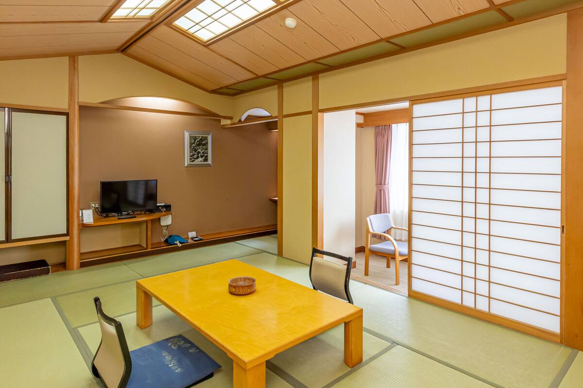 A traditional Japanese room with tatami flooring, a wooden table, a television, and sliding doors.