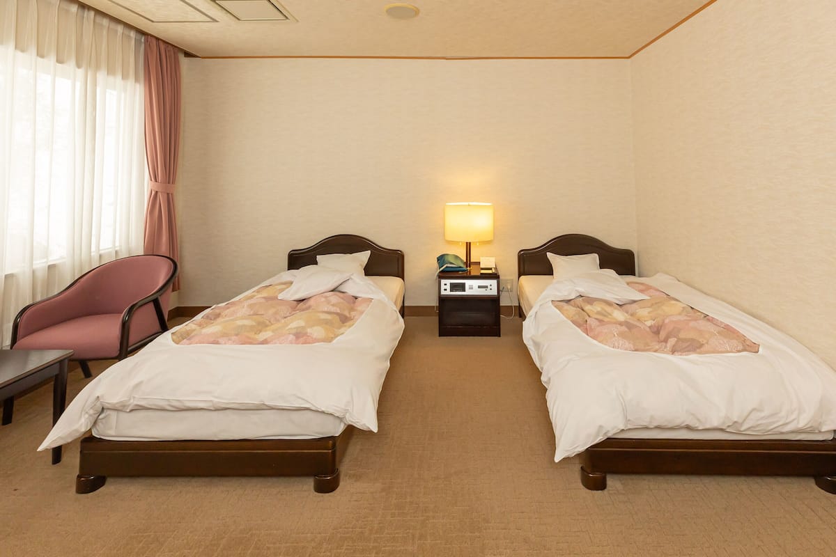 A hotel room with two beds, a chair, a nightstand, and a lamp.