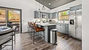 Una cocina moderna con una isla central, taburetes de bar, electrodomésticos de acero inoxidable y vistas al exterior.