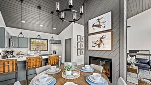 Una cocina moderna con gabinetes grises, un comedor con mesa de madera dispuesta para cuatro personas y una chimenea.