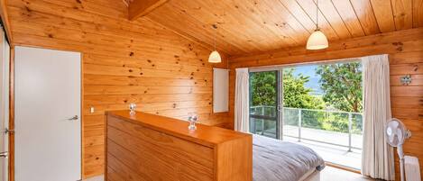 Une chambre dans un chalet en bois, comprenant un lit, une commode, une porte-fenêtre coulissante donnant sur un balcon et un ventilateur de plafond.