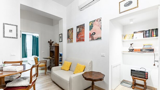 Una sala moderna con sofá, mesa de comedor, sillas, una pequeña mesa redonda y una estantería.