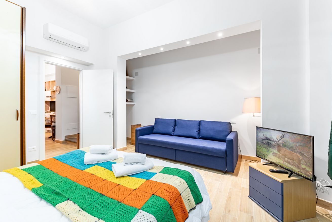 Un dormitorio con una cama, un sofá azul, un televisor y un armario.