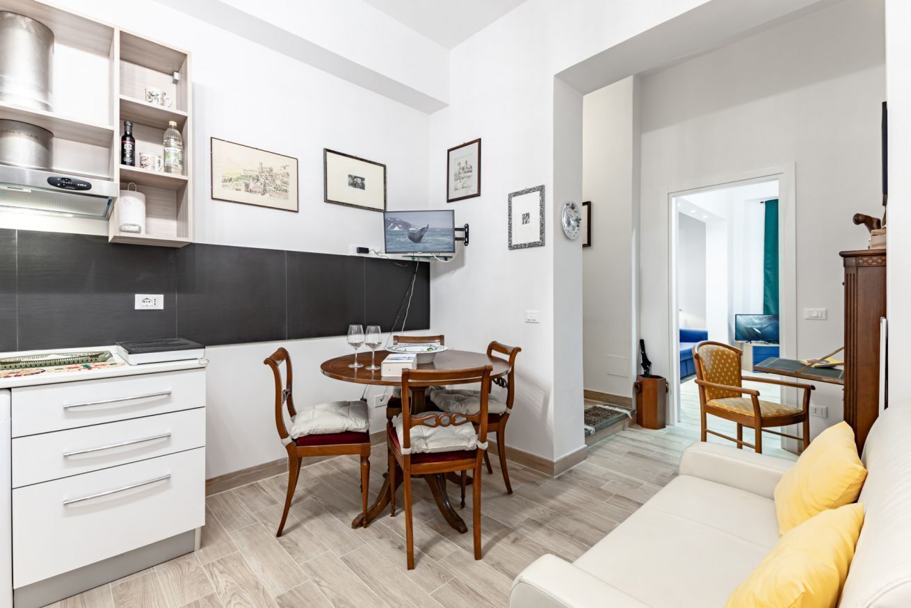 Una cocina moderna con comedor, muebles blancos y un televisor de pantalla plana.