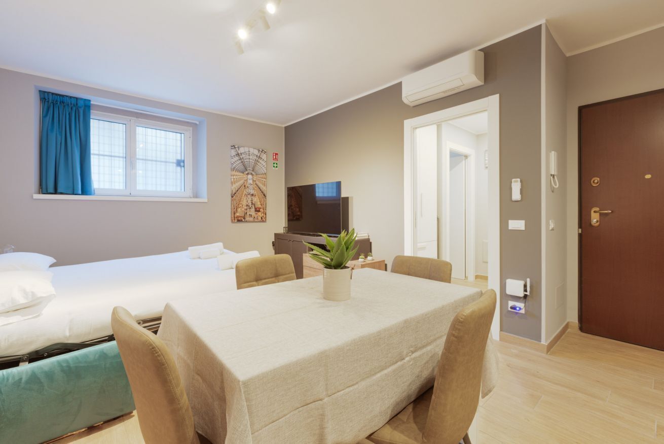 Una camera d'albergo con un letto, un tavolo da pranzo con sedie, una TV e una finestra con tende.