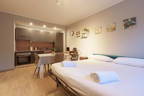 A modern hotel room with a bed, a desk, a kitchenette, and a dining area. - GuestHost - Cozy and modern 30sqm studio apartment, able to comfortably accommodate up to 2 people, located in the basement of a building WITHOUT a lift (steps to access it). The apartment is located in a strategic position, just a 5-minute walk from the (Milano)