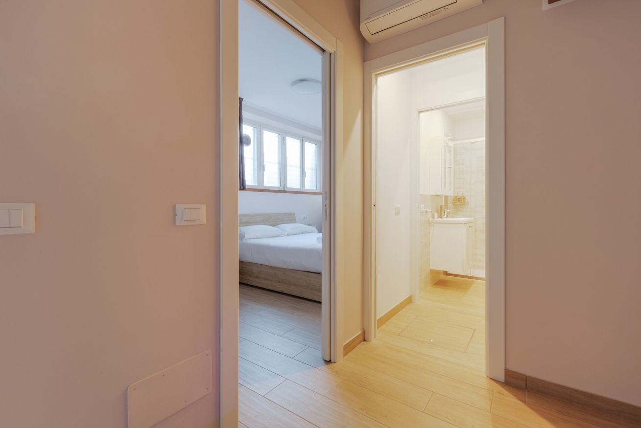 Un pasillo que lleva a un dormitorio con cama y un baño con lavabo y espejo.