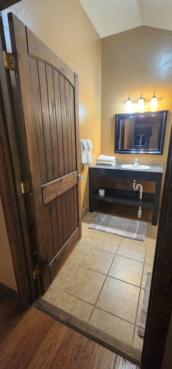 A bathroom with a wooden door, a sink, a mirror, and a towel rack. - Circle R Cabin 4, Private Ranch, Mountain Views (East Glacier)