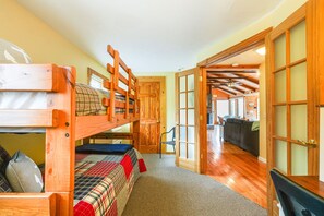 Una cama litera con cubrecama a cuadros, una puerta de madera y vistas a una sala de estar con un sofá y una cocina.