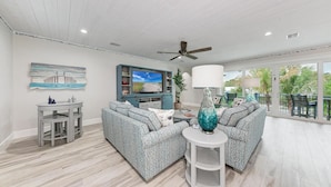 A spacious living room with a large TV, two sofas, a coffee table, and a ceiling fan. - No R-Egrets:1 Block to Beach! Pool Game Room by Anna Maria Life Vacation Rentals (Holmes Beach)
