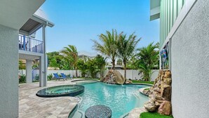 A swimming pool with a waterfall feature, surrounded by palm trees and a stone wall. - No R-Egrets:1 Block to Beach! Pool Game Room by Anna Maria Life Vacation Rentals (Holmes Beach)
