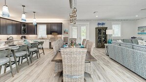 A spacious kitchen with dark cabinets, a central island, and a dining area with wicker chairs. - No R-Egrets:1 Block to Beach! Pool Game Room by Anna Maria Life Vacation Rentals (Holmes Beach)