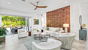 A spacious living room with a large window, a ceiling fan, and a wooden wall panel. - Tamiami Vice - Luxury Siesta Key Home with Heated Pool & Prime Location – Book Your Escape Today! (Sarasota)