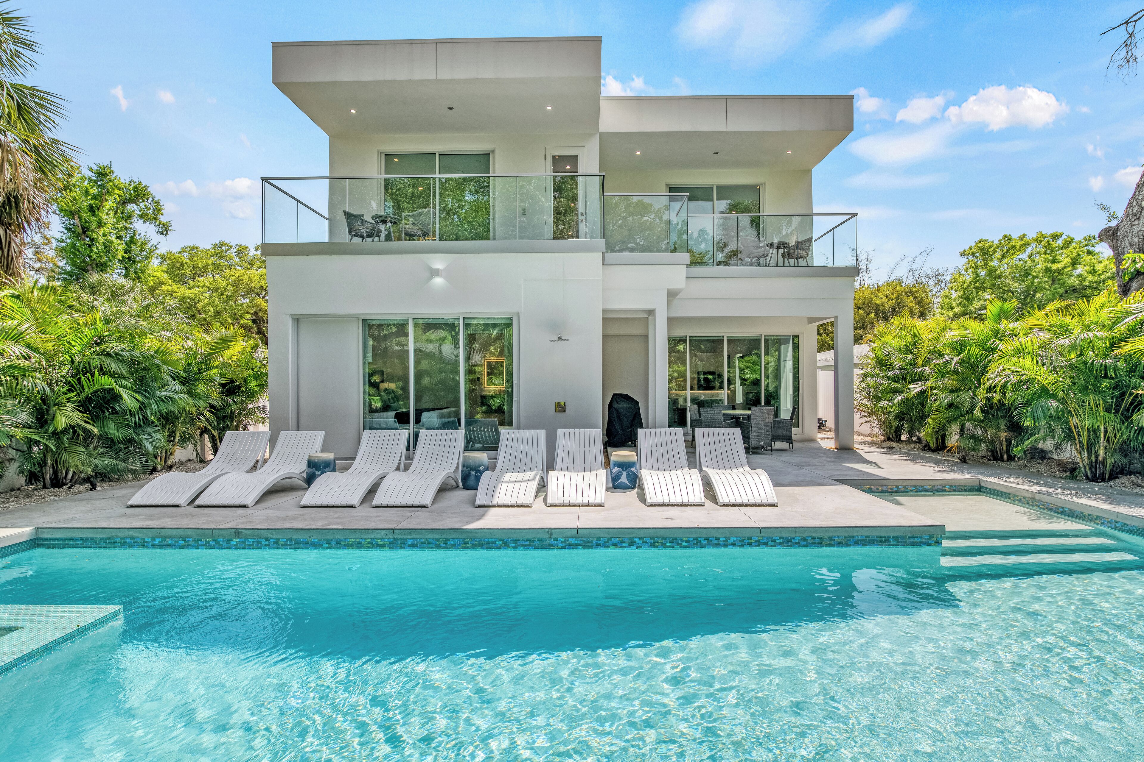 Une maison moderne à deux étages, dotée d’une piscine, de chaises longues et d’une végétation luxuriante.