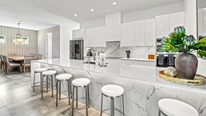 A modern kitchen with a marble island, bar stools, and a dining area with a wooden table and chairs. - Tamiami Vice - Luxury Siesta Key Home with Heated Pool & Prime Location – Book Your Escape Today! (Sarasota)