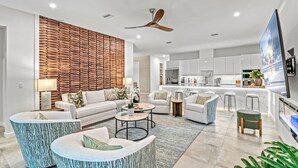 A modern living room with a sofa, coffee table, and chairs, a kitchen area with white cabinets, and a ceiling fan. - Tamiami Vice - Luxury Siesta Key Home with Heated Pool & Prime Location – Book Your Escape Today! (Sarasota)