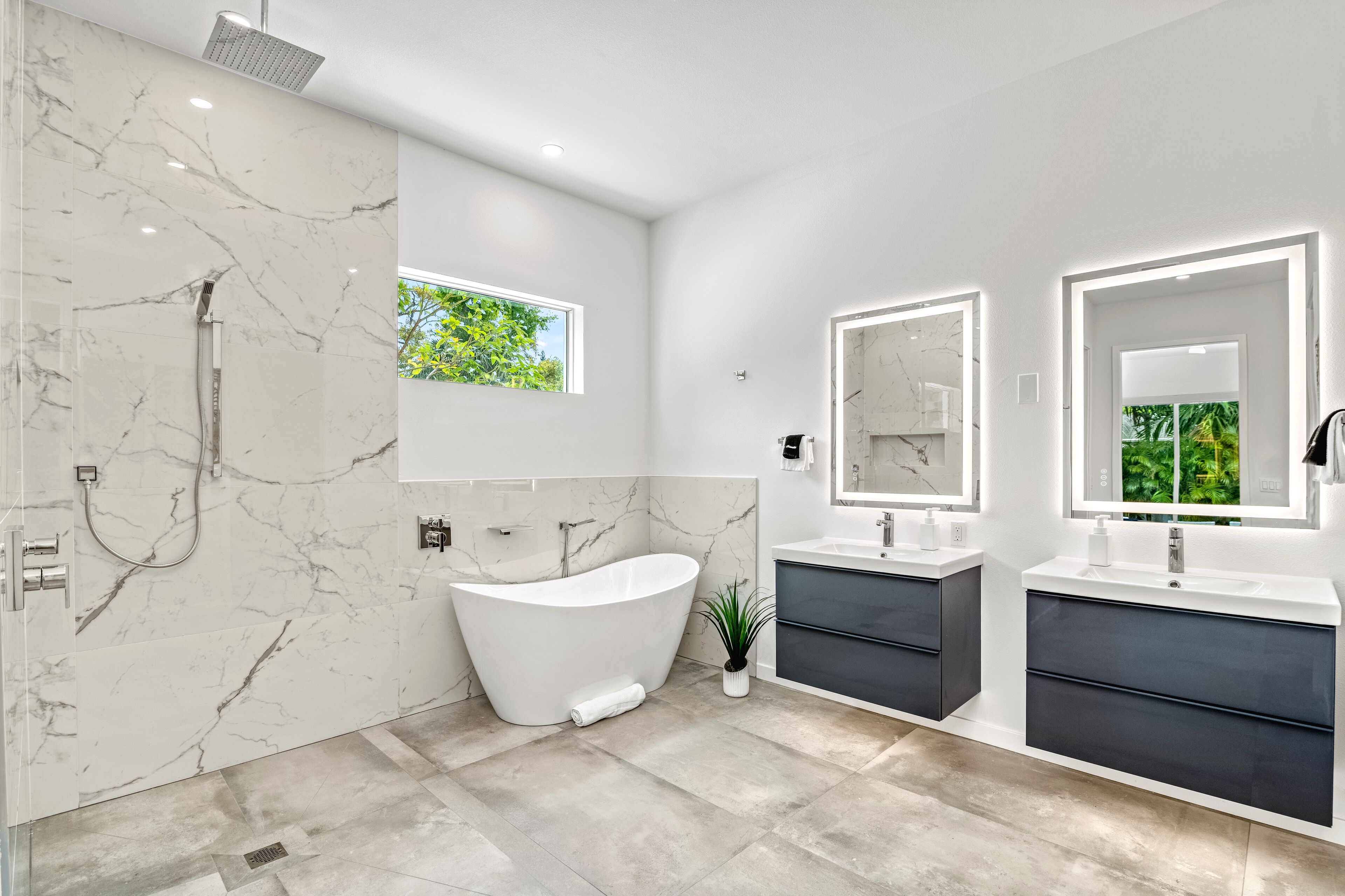 Een moderne badkamer met een vrijstaand bad, twee wastafels en marmeren wanden.