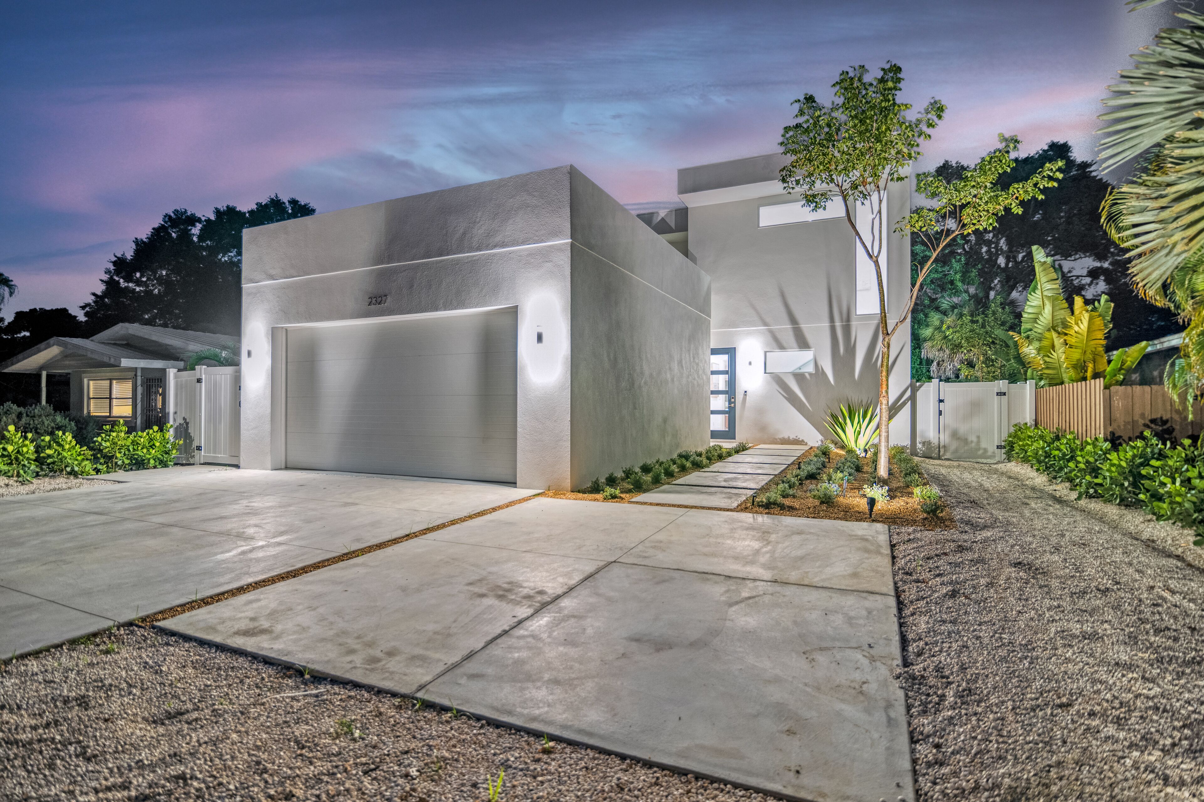 Une maison moderne avec un grand garage, un jardin bien entretenu et un ciel dégagé.