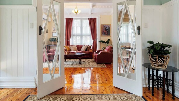 Ein geräumiges Wohnzimmer mit Holzboden, einer roten Sofagarnitur und einer Glastür zu einem weiteren Raum.