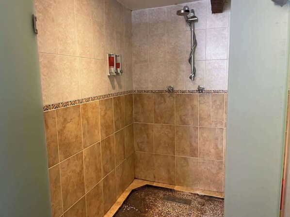 Un área de ducha pequeña con azulejos, cabezal de ducha de mano y grifo empotrado en la pared.