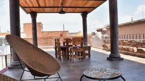 An outdoor patio with a wooden table and chairs, a wicker chair, and a tiled table.