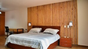 A bedroom with a wooden slat wall, a bed with striped bedding, a nightstand with a lamp, and a desk with a chair.