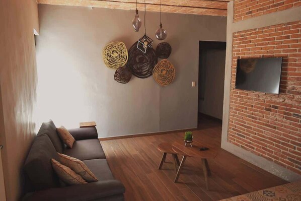Una sala de estar moderna con un sofá, una mesa de centro y un televisor instalado en una pared de ladrillo.
