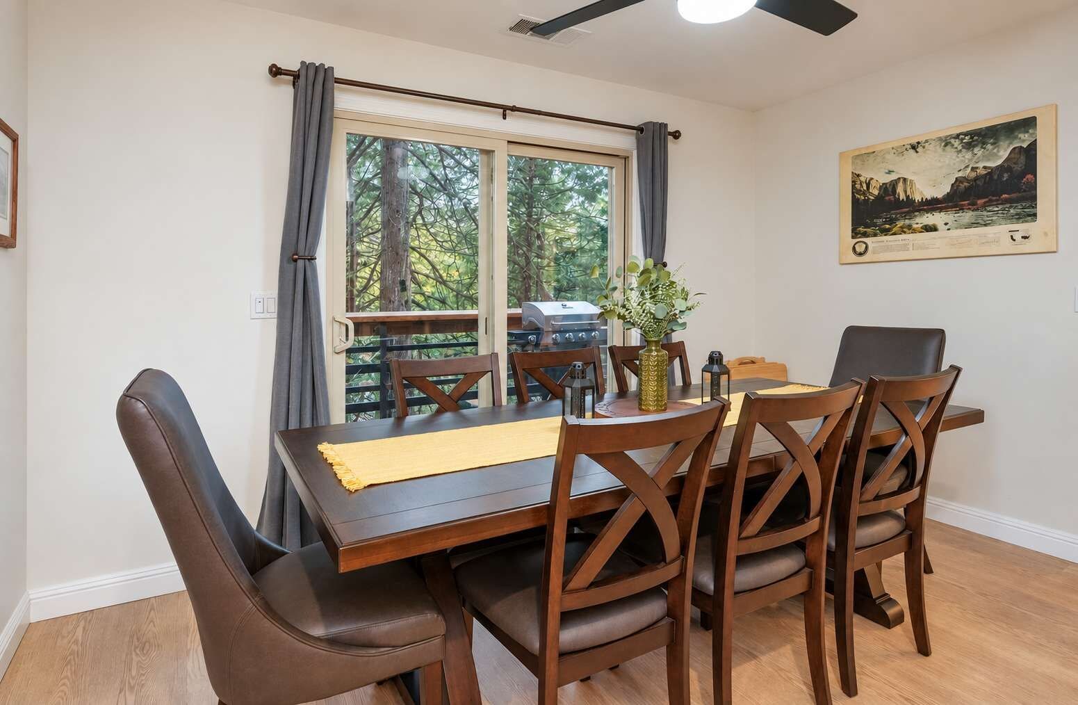 A dining area with a table set for four, wooden chairs, a vase with greenery, and a painting on the wall.