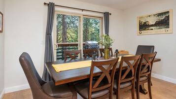 A dining area with a table set for four, wooden chairs, a vase with greenery, and a painting on the wall.