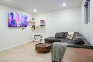 Een woonkamer met een grijze bank, een salontafel, een flatscreen-televisie en een kleine plant op een plank.