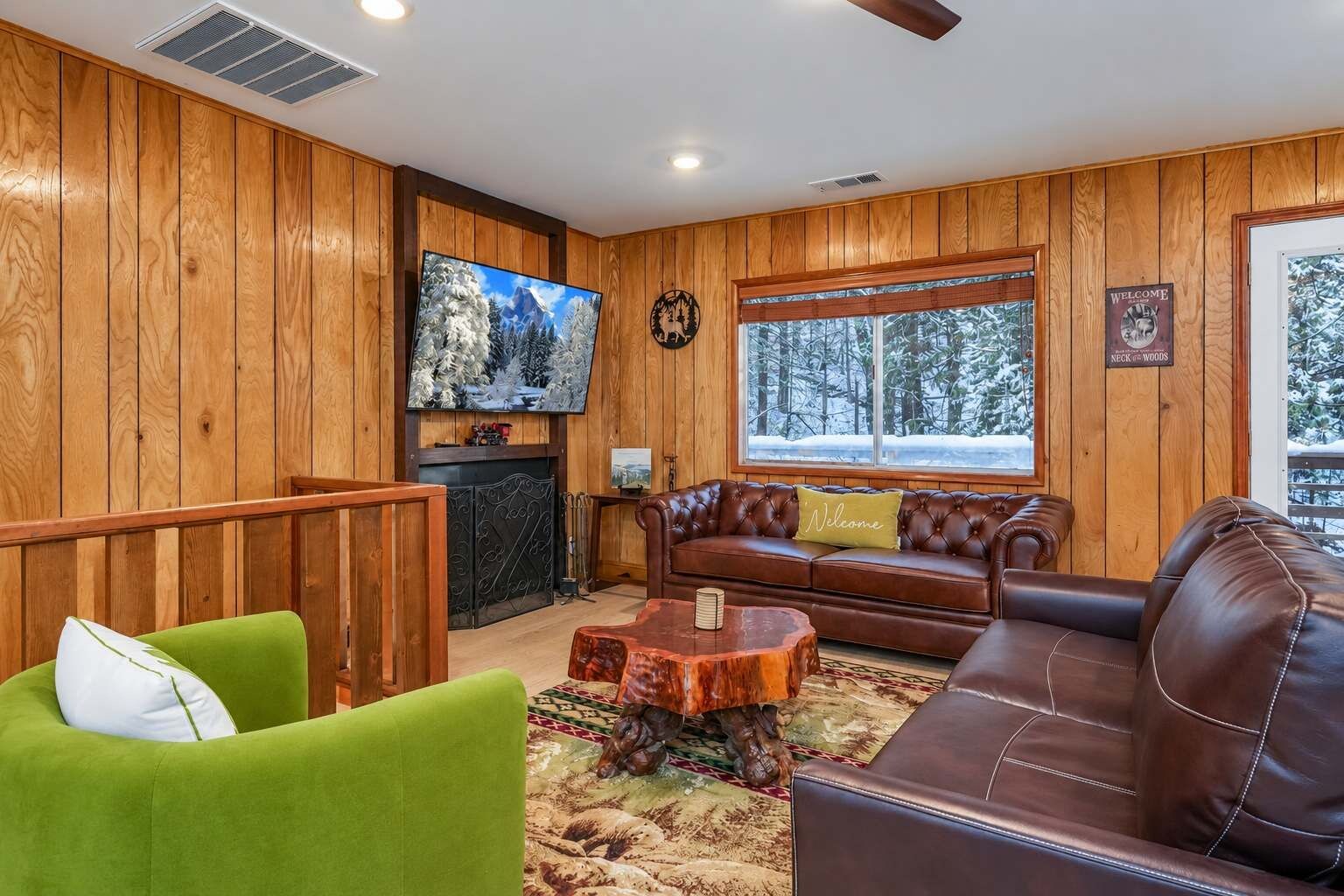 A cozy living room with wooden paneling, a fireplace, a television, and a large window with a snowy view.