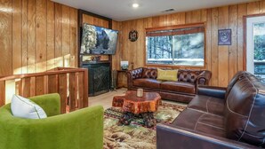 A cozy living room with wooden paneling, a large flat-screen TV, a fireplace, and a window with a snowy view.