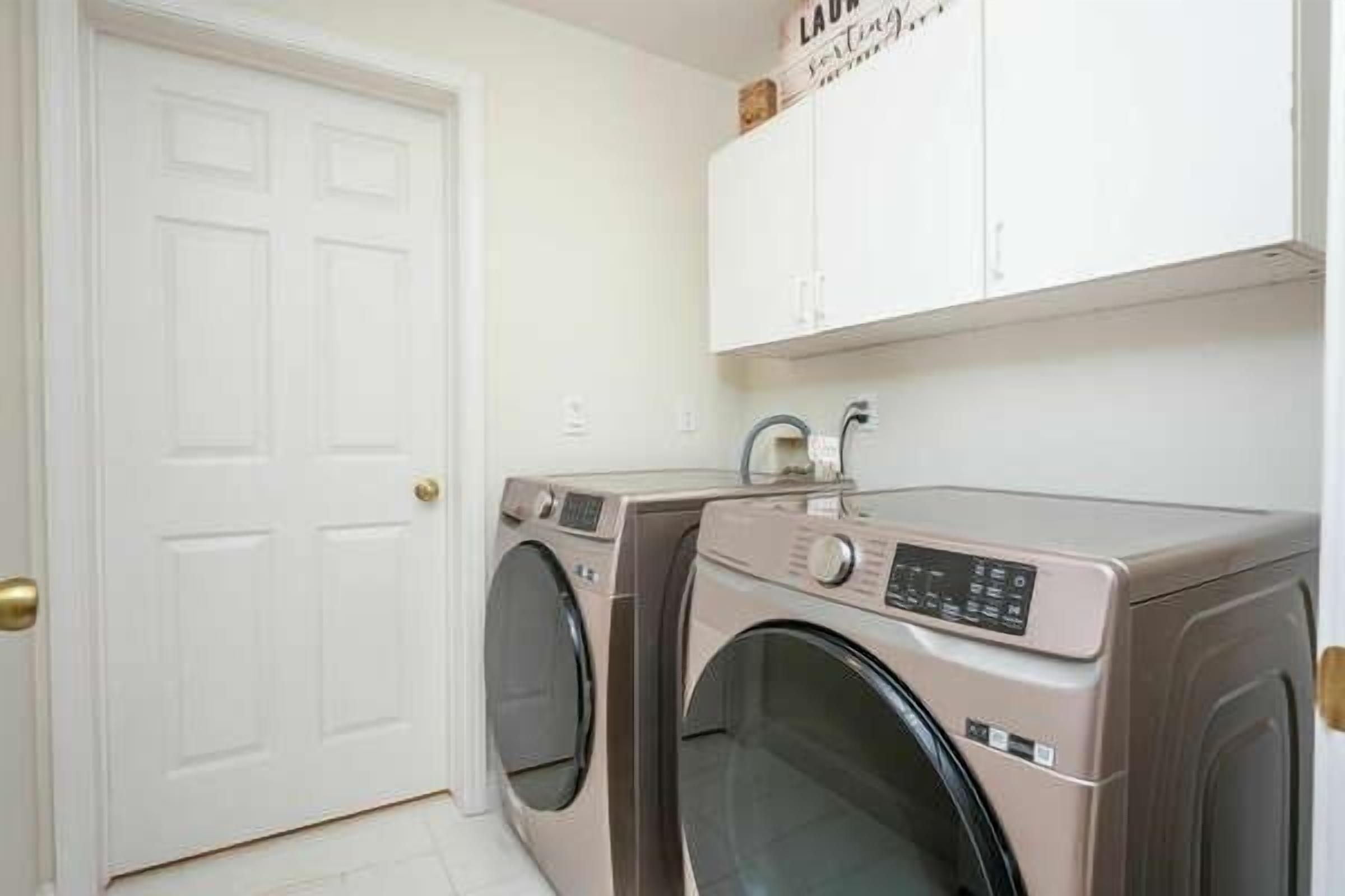 A laundry room with two washing machines, a white door, and a cabinet above the machines.