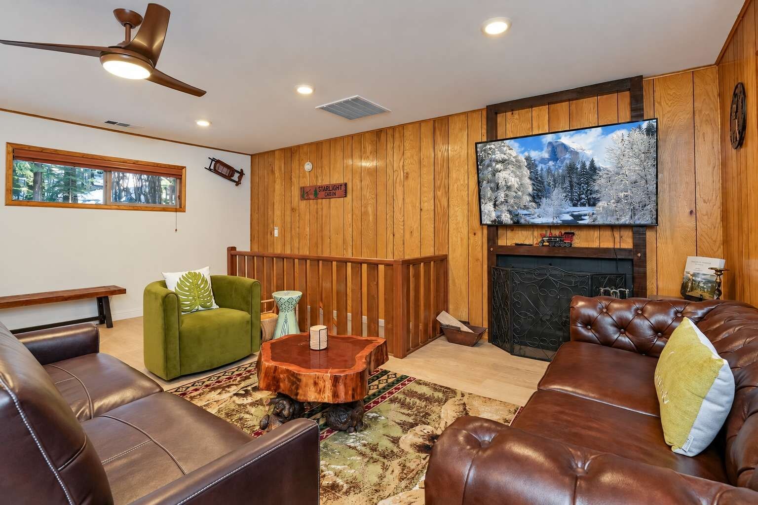 A cozy living room with a fireplace, a television mounted on the wall, and a wooden ceiling fan.