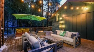 An outdoor deck with a sofa, chairs, and a table, surrounded by a wooden deck and a stone wall.