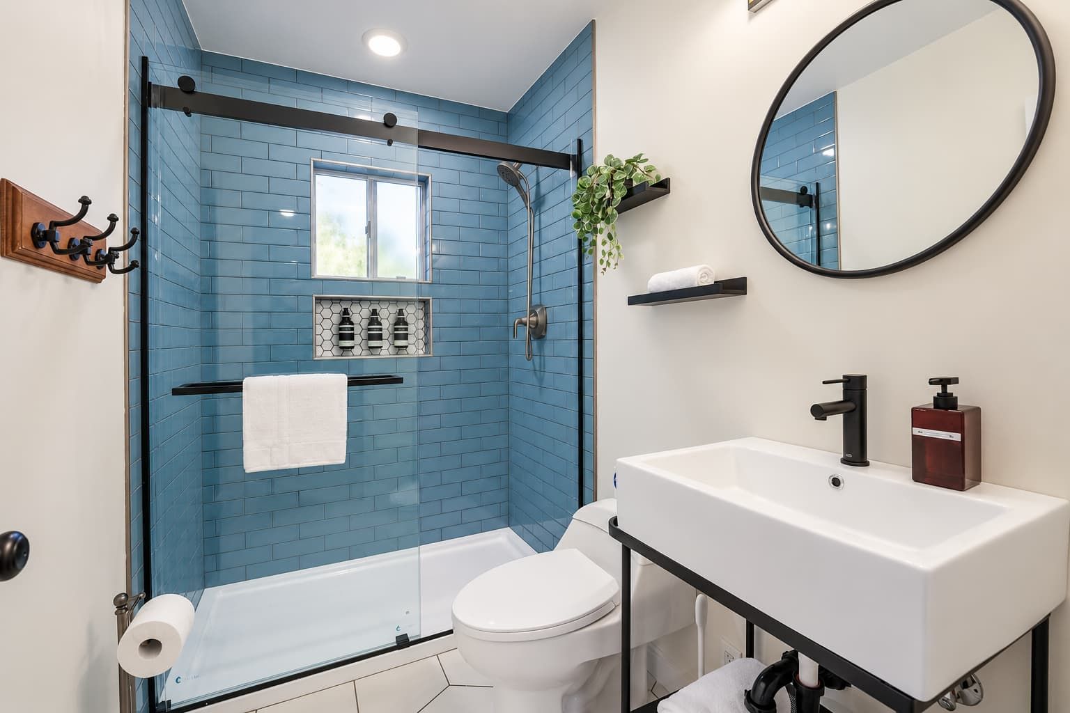 A modern bathroom with a glass-enclosed shower, a white toilet, a white sink with a black faucet, and a mirror above the sink.