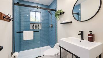 A modern bathroom with a glass-enclosed shower, a white toilet, a white sink with a black faucet, and a mirror above the sink.