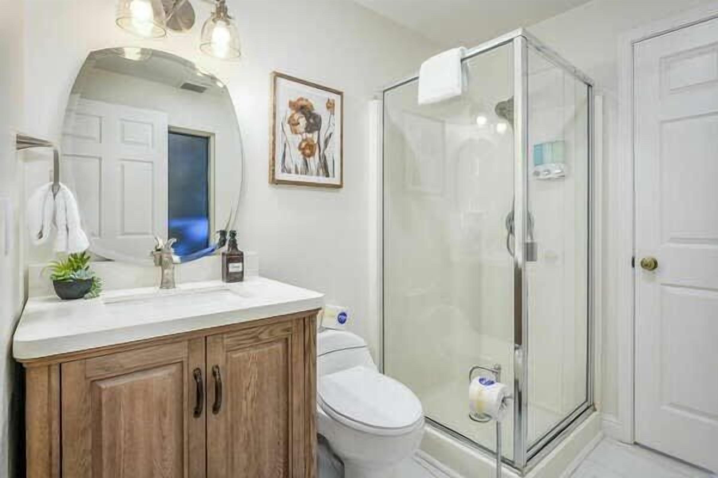A bathroom with a wooden vanity, a toilet, a glass shower enclosure, and a framed picture on the wall.