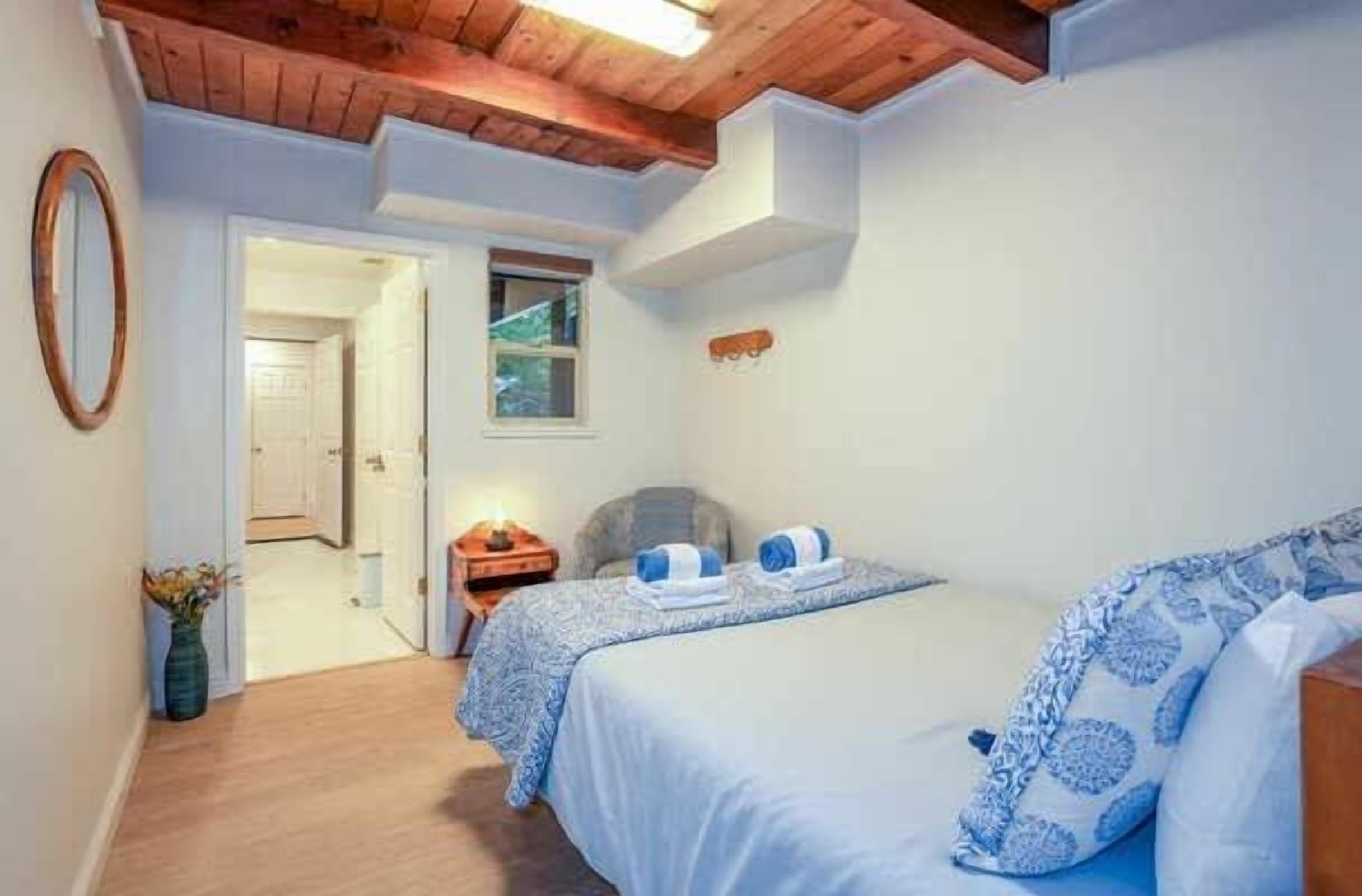 A bedroom with two beds, wooden ceiling beams, a small bedside table, and a nightstand.