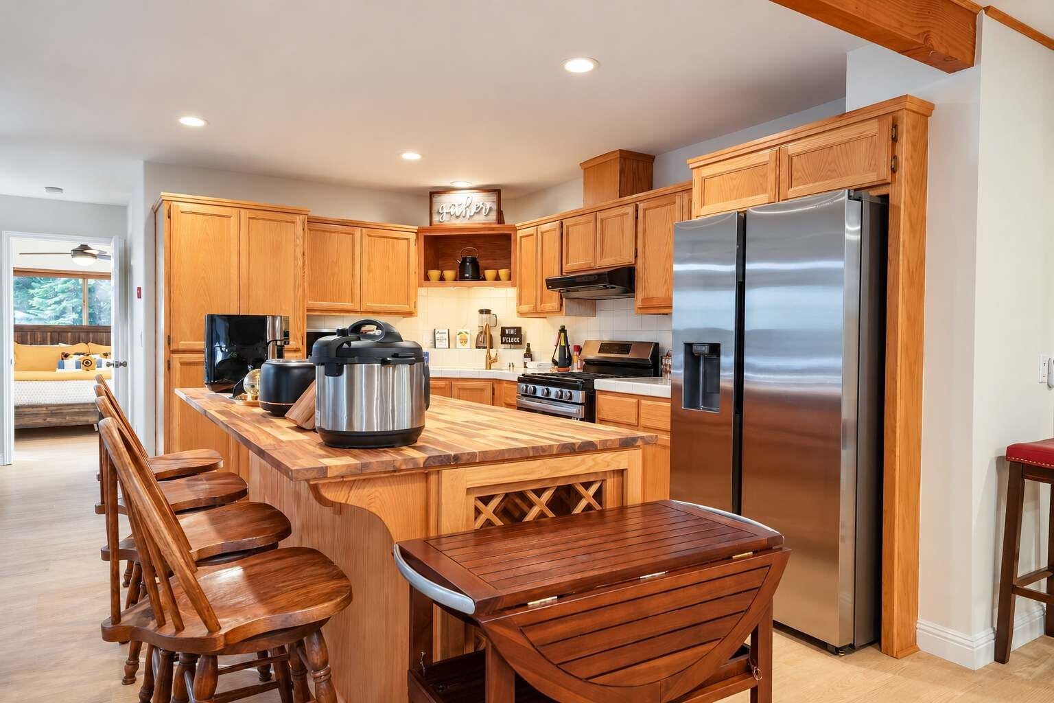 A modern kitchen with wooden cabinets, a stainless steel refrigerator, a large island with bar stools, and a built-in oven.